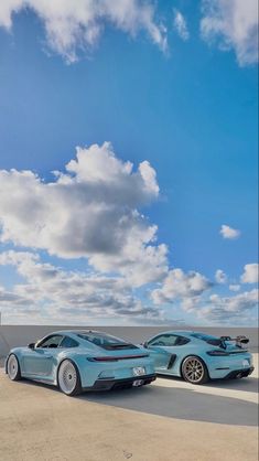 two blue sports cars parked next to each other in front of the sky with clouds