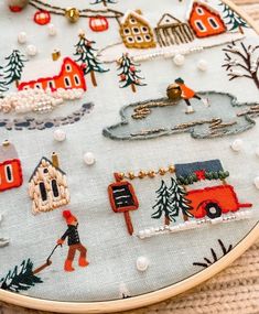 a close up of a cross stitch on a piece of cloth with houses and trees