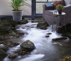 a living room with a couch, chair and water stream running through the floor next to a window