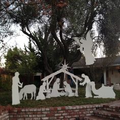 a nativity scene is displayed in front of a brick wall and tree with white paper cutouts