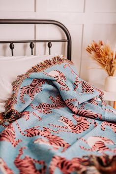 a bed with a blue and pink bedspread next to a white vase filled with dried flowers