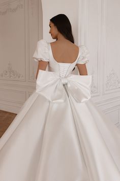 a woman in a white wedding dress with a big bow on the back of it