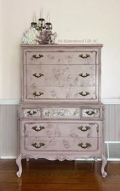 an old dresser painted in pink and white with flowers on the top, next to a candle holder