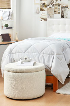 a white bed sitting next to a wooden foot stool on top of a hard wood floor