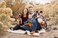 a man, woman and baby are sitting on a blanket in the desert with their dogs