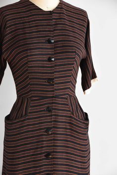 "Vintage 1950s cotton fitted dress. Vertical black and orange stripes. High collar, longer capped sleeves, seamed bust and nipped waist. Straight skirt with front pockets. Stream of front buttons for closure. State of garment | excellent Measurements ✂--- best fit | small bust | 35\" shoulders | not specified shoulder to waist | 15.5\" sleeves | not specified waist | 25-26\" hips | up to 39\" total length (shoulder to hem) | 39 \" ★★Visit The Shop★★ http://www.etsy.com/shop/seaofvintage ➸ Find t Short Sleeve Dresses With Vertical Stripes For Work, Classic Striped Cotton Dress, Classic Striped Dresses For Daywear, Fitted Short Sleeve Dress With Striped Collar, Fitted Short Sleeve Dress With Vertical Stripes, Fitted Dress With Vertical Stripes And Short Sleeves, Vintage Striped Fitted Dress, Retro Fitted Dress With Vertical Stripes, Fitted Retro Dresses With Vertical Stripes