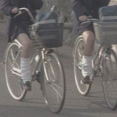 two people riding bikes with baskets on the front and back wheels, one person wearing white socks