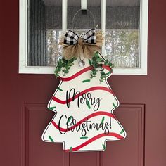 a merry christmas sign hanging on the front door with a bow around it's neck