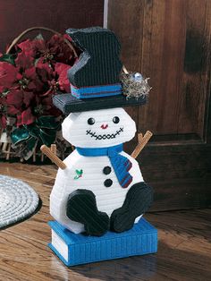 a knitted snowman sitting on top of a wooden table next to a potted plant