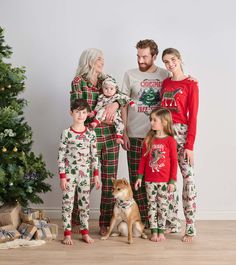 a family wearing matching christmas pajamas standing in front of a christmas tree with their dog