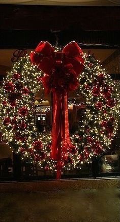 a large wreath with red bows and lights in front of a store window at night