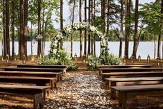 an outdoor ceremony setup with wooden benches and flowers on the aisle, surrounded by trees