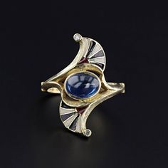 A striking Egyptian Revival ring (circa 1910) with black white and red enamel and a natural blue sapphire at its center.  Two tiny diamonds add a glittery flourish on each point of the ring.  The sapphire cabochon is moderate blue in color and weighs approximately 2.16ct.   The face of the 18k gold ring measures 1 inch tall by 0.4 inches wide, and it is in great condition.  The ring is a size 6.75, but it can be resized free of charge.  It weighs 6.14 grams.  We have many other fantastic offerin Art Deco Enamel Rings For Formal Occasions, Art Deco Yellow Gold Enamel Ring For Formal Occasions, Art Deco Enamel Ring As A Gift, Art Deco Enamel Ring As Gift, Elegant Blue Enamel Ring With Gemstone, Art Deco Formal Yellow Gold Enamel Ring, Formal Yellow Gold Art Deco Enamel Ring, Formal Art Deco Yellow Gold Enamel Ring, Formal Enamel Ring With Gemstone