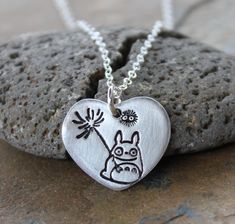 "This necklace features a handmade fine silver (99.9% pure silver) heart pendant stamped with a sweet little Totoro with a flower and a friendly soot sprite. The stamping is oxidized to make it stand out and the rest of the pendant is matte silver. The heart charm is about 7/8\" wide and 3/5\" tall (22x18mm) and is hung on a delicate sterling silver chain finished off with a sterling silver lobster clasp. I have a few other Totoro themed items in my shop. See them here: https://www.etsy.com/shop Anime Fan Art, Soot Sprite, Silver Jewelry Diy, Cleaning Silver Jewelry, Forest Spirit, Precious Metal Clay, Handmade Heart, Silver Heart Pendant, Silver Jewellery Sets