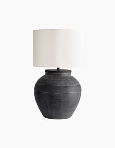 a black vase with a white shade on it's side and a light in the middle