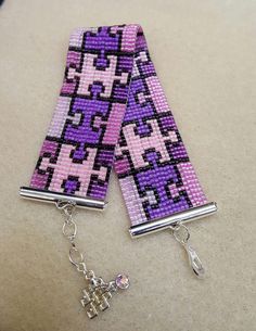 two purple and black squares are attached to silver chains with a cross on each side