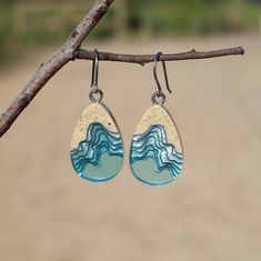 the earrings are hanging from a tree branch with blue and white waves on it,