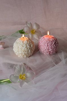 three candles are sitting on a white cloth with tulle and flowers in the background