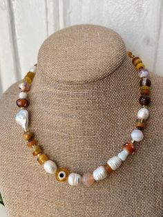 Made in Harlem, inspired by our parks, nature and the life daily grind. This is a one of kind piece, beaded necklace with a large yellow glass evil eye, mix of semi precious stones, glass brown capped mushroom and large beautiful natural freshwater pearls.  This has become an unintentional signature style i love to make. I love to blend the earthy warm colors i see Al day with the semis precious  gemstones contrasting the beautiful genuine freshwater pearls. And the highlight the evil eye for protection. Gold plated clasp closure 16'' inches Handmade Crystal Necklaces With Round Beads For Everyday, Spiritual Handmade Beaded Necklace For Everyday, Handmade Orange Necklace For Everyday, Handmade Amber Beaded Necklaces For Festivals, Handmade Amber Beaded Necklace For Festivals, Unique Yellow Jewelry For Everyday, Festival Handmade Amber Beaded Necklaces, Handmade Amber Beaded Necklace For Healing, Handmade Yellow Necklace For Everyday Wear