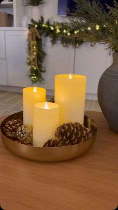 three lit candles on a tray with pine cones