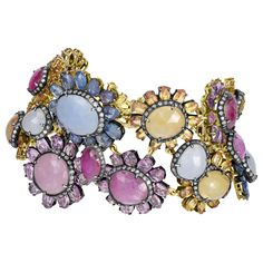 Introducing our breathtaking Victorian 110 Cttw. Sapphire, Ruby, and Diamond Link Bracelet, a true masterpiece of elegance and sophistication. This stunning bracelet features a captivating collection of floral motifs adorned with vibrant sapphires in shades of blue, pink, and yellow. Each floral motif showcases a round or oval sapphire at its core, encircled by a halo of shimmering diamonds set on a backdrop of black rhodium. These motifs are intricately linked together with oval rubies, creatin Elegant Multi-stone Bangle Bracelets, Luxury Multi-stone Bracelet, Luxury Jeweled Bangle, Luxury Diamond Bracelet With Jewels, Luxury Yellow Gold Bracelets With Rose Cut Diamonds, Fine Jewelry Multicolor Wedding Bracelet, Multicolor Fine Jewelry Bracelet For Wedding, Luxury Multicolor Bracelet Jewelry, Elegant Multicolor Diamond Bracelet