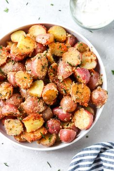 a white bowl filled with potatoes covered in seasoning and sprinkled with parsley