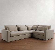 a beige sectional couch sitting on top of a hard wood floor next to a white wall