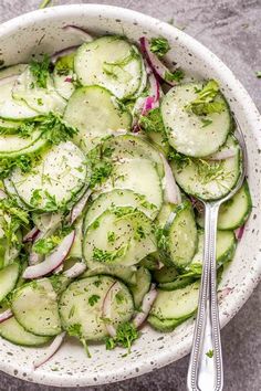 a bowl filled with cucumbers, onions and herbs next to two spoons