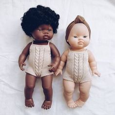 two dolls are laying next to each other on a white sheet, one is black and the other is brown