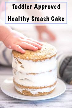 a toddler's hand on top of a healthy smash cake with white frosting