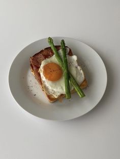 a white plate topped with an egg and asparagus covered in bacon on toast