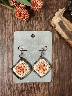 a pair of earrings sitting on top of a wooden table next to a pine cone