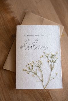 a greeting card with wildflowers on it sitting on top of a wooden table