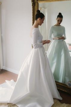 a woman in a wedding dress looking at her reflection in a mirror while another woman stands nearby