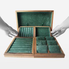 two hands are holding an open wooden box with green velvet linings on the inside