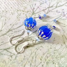 two blue glass beaded earrings with silver hooks on a floral fabric tablecloth background