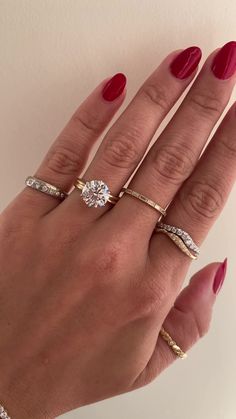 a woman's hand with three different rings on her fingers and two red nail polishes