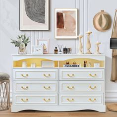 a white dresser with yellow drawers and pictures on the wall above it in a living room