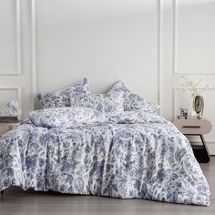 a bed with blue and white comforters in a room next to a table on which is a vase