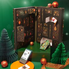 an open book with christmas decorations and ornaments around it on a green tableclothed surface