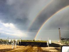 two rainbows in the sky over a dirt road