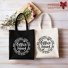 two black and white shopping bags sitting on top of a wooden table next to flowers