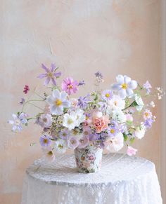 a white table topped with a vase filled with lots of different colored flowers next to a wall