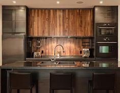 a kitchen with an island, sink and oven in the center is surrounded by bar stools