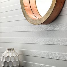 a white vase sitting next to a wall with a circular mirror on it's side