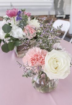 two vases filled with flowers sitting on top of a pink tablecloth covered table