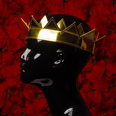 a black mannequin head with a gold crown on it's head against a red background