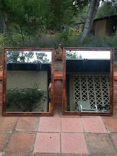 two mirrors sitting on top of a brick wall next to each other in front of trees