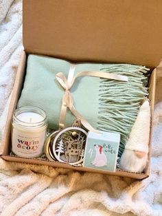 an open box with candles, towels and other items in it on a white blanket