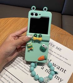 a person holding up a phone case with owls and fish decorations on the front, while sitting at a table